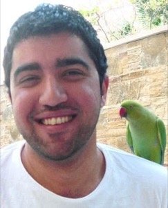 Photo of Ali smiling with a green parakeet on his shoulder